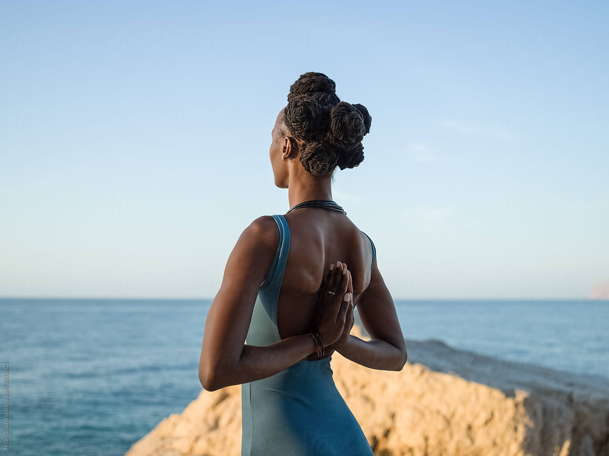 Black woman clasping hands behind back against sea
