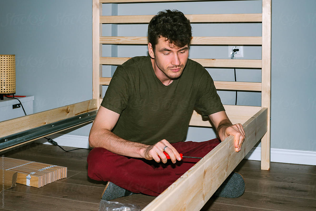 Man enthusiastically assembles a wooden bed