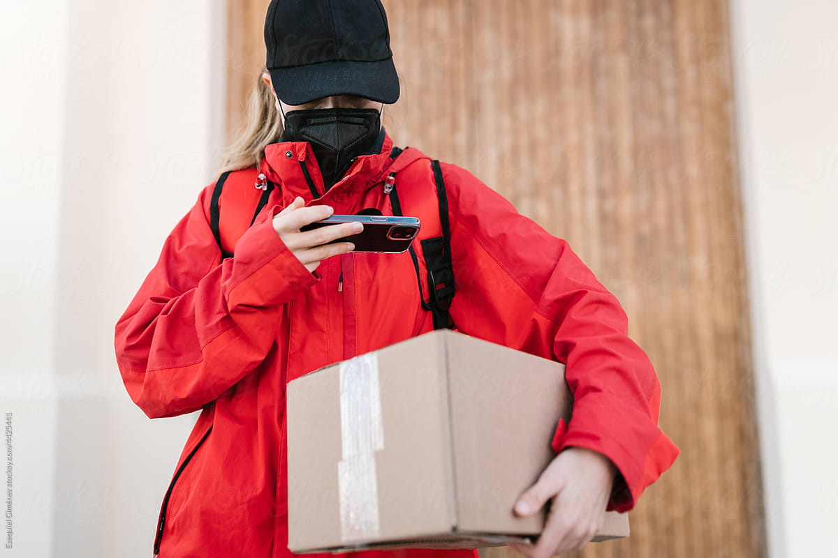 Female delivery worker with box using smartphone