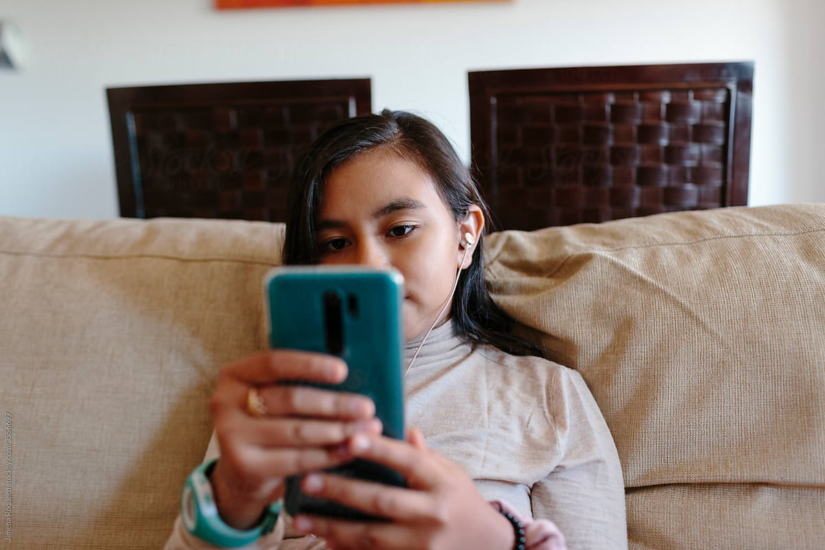 Hispanic 10 year old girl with mobile phone on the couch indoors