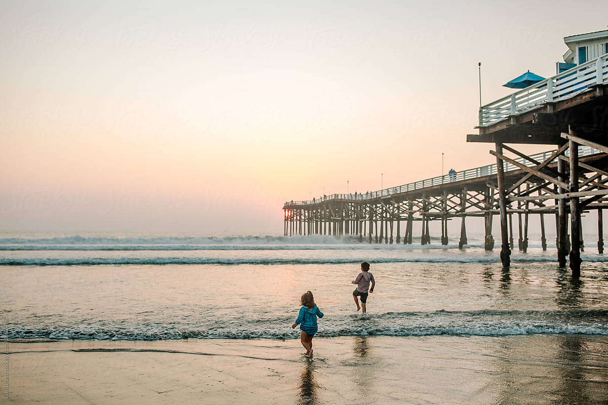 Young siblings in ocean near pier at sunset