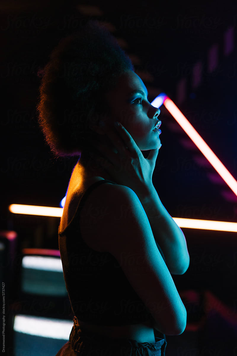 Dreamy black woman touching face in neon illumination
