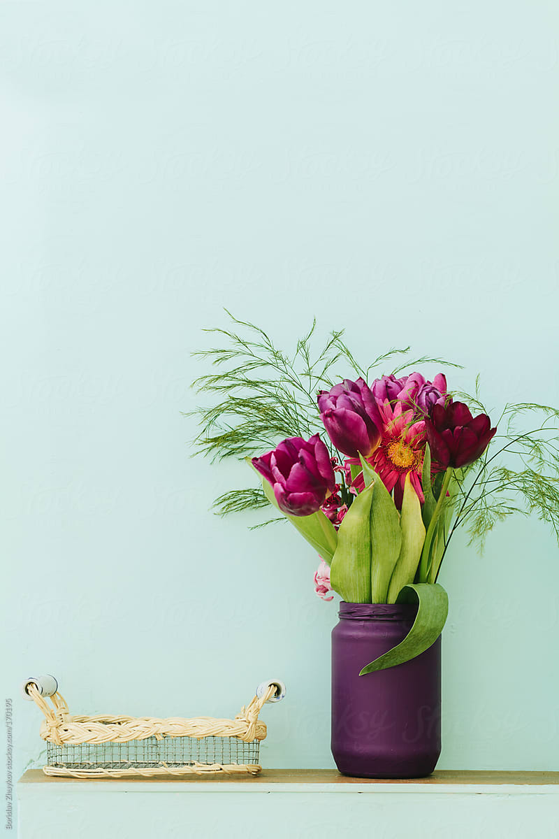 Beautiful purple vase with flowers and handmade tray on bluish wall