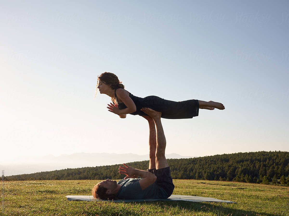 Man and woman practicing Free Bird pose on lawn