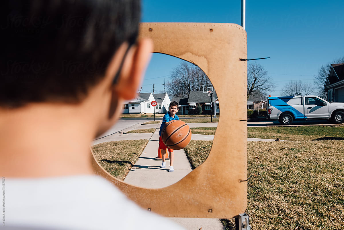 Boy bouncing basketball through hoop on sidewalk.