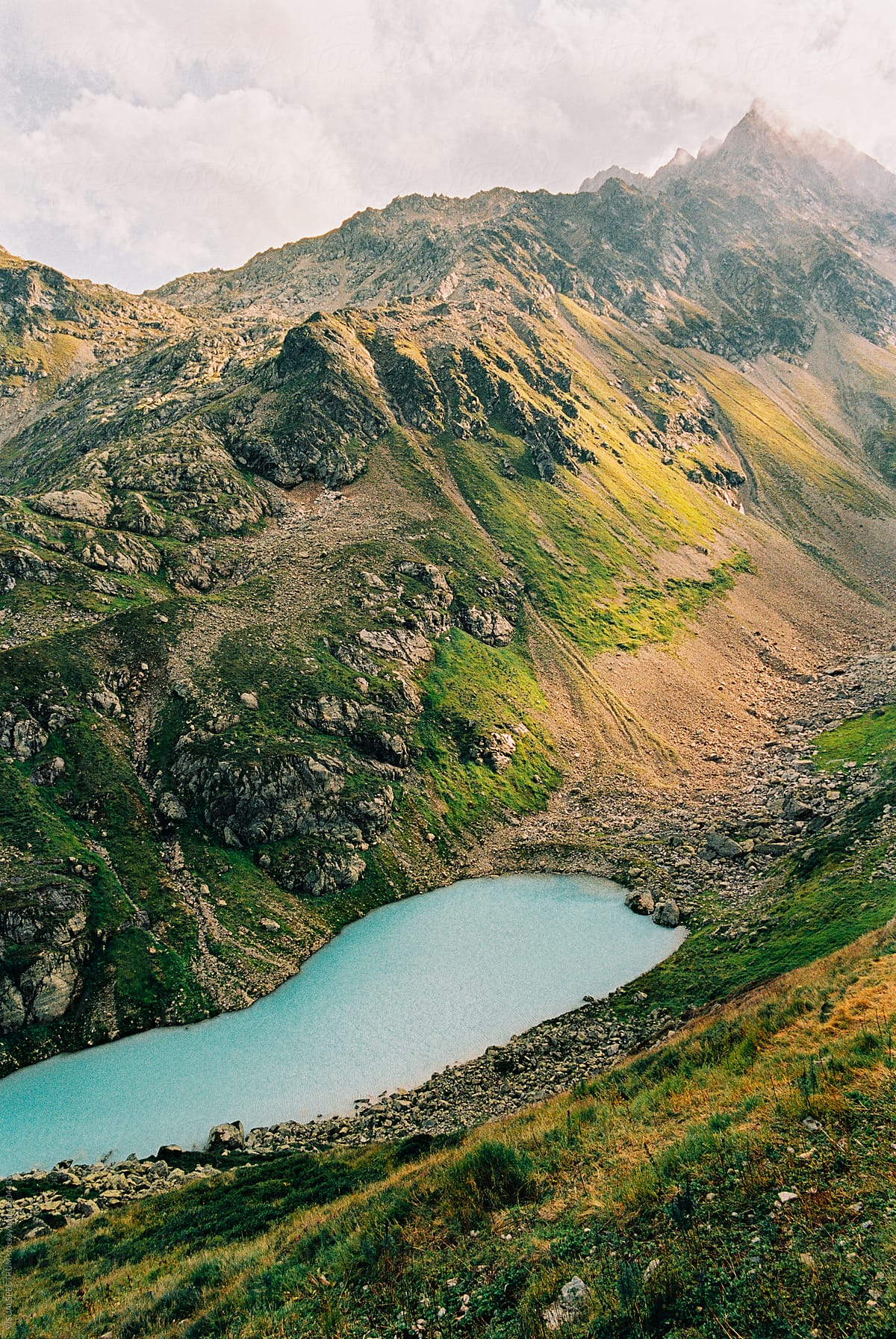 "Turquoise Alpine Lake Surrounded By Peaks In Warm Morning Light" by