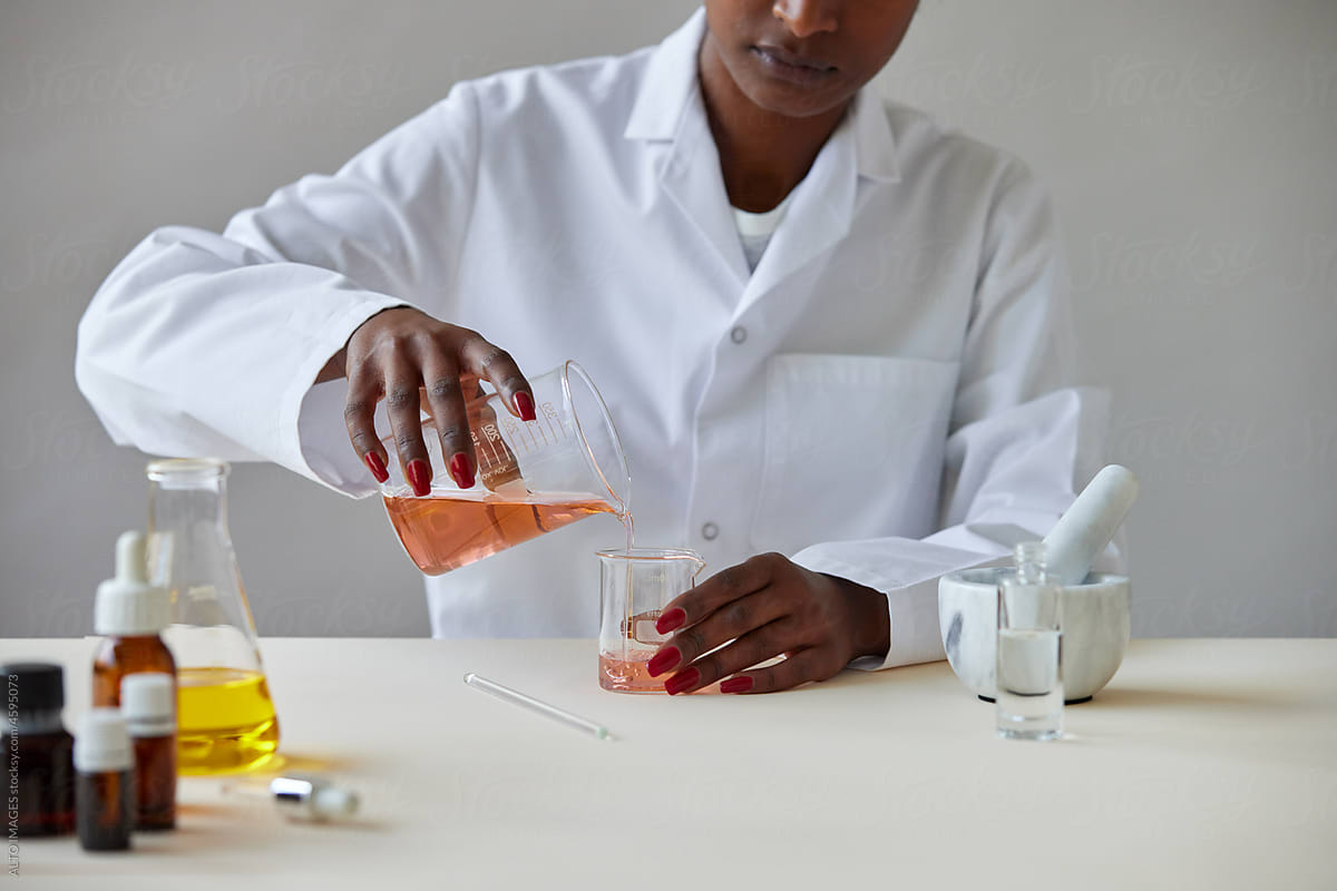 Anonymous black pharmacist pouring chemical liquid