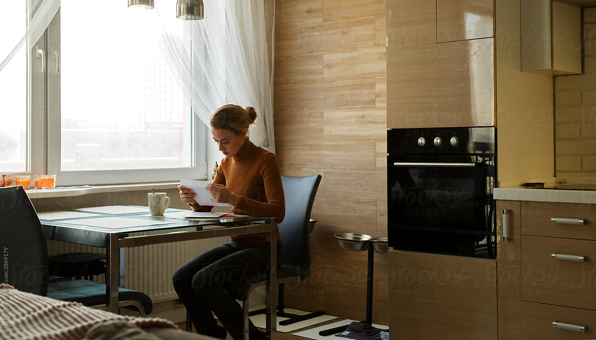 Serious woman reading letter at table in kitchen
