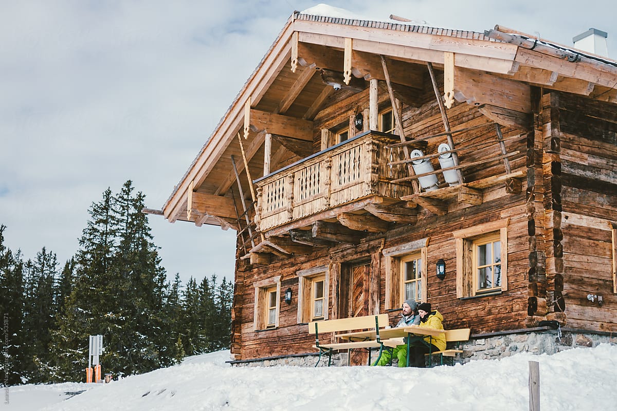 couple sitting at an alpine cabin on a bench in snowcovered mountain landscape
