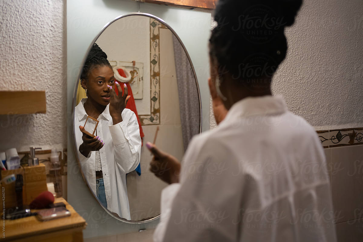 Black Woman Making Up In Front Of The Mirror At Home By Stocksy