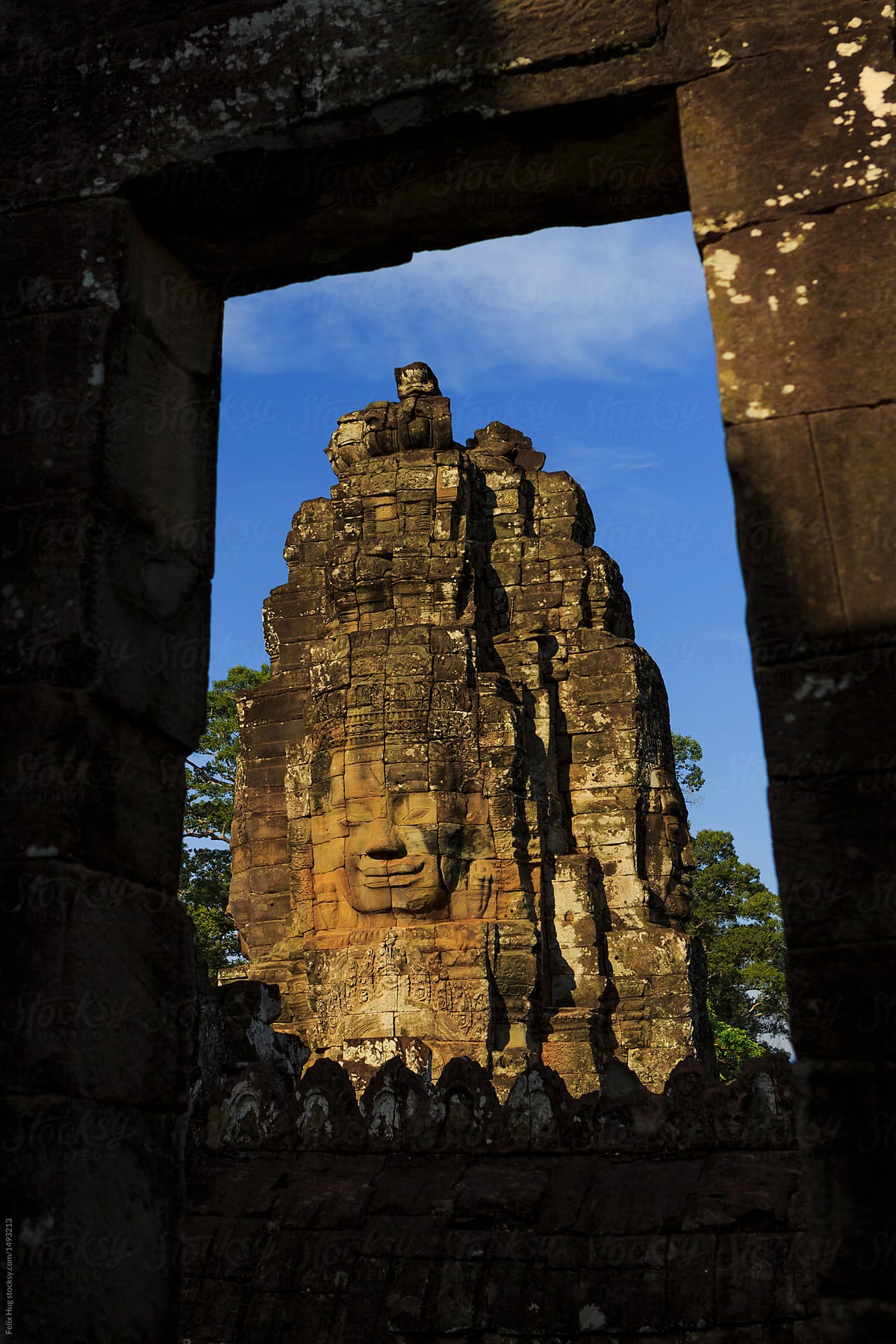 the famous stone faces of the Bayon Temple at Angkor Wat . The view is framed by a stone window
