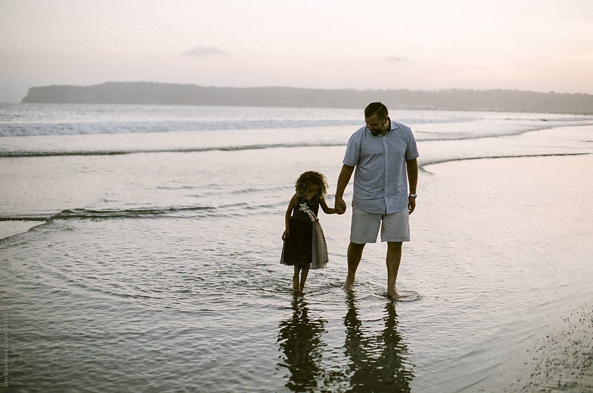 Dad and daughter wading in ocean at sunset