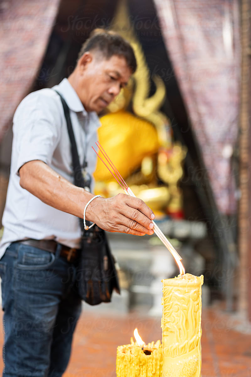 Thai man lighting incense in temple.