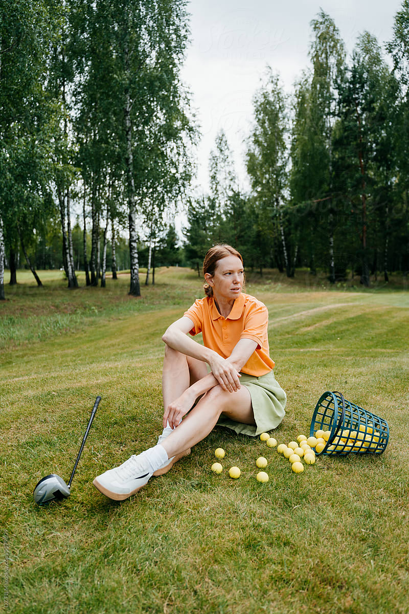 A woman is sitting on the lawn next to the golf equipment
