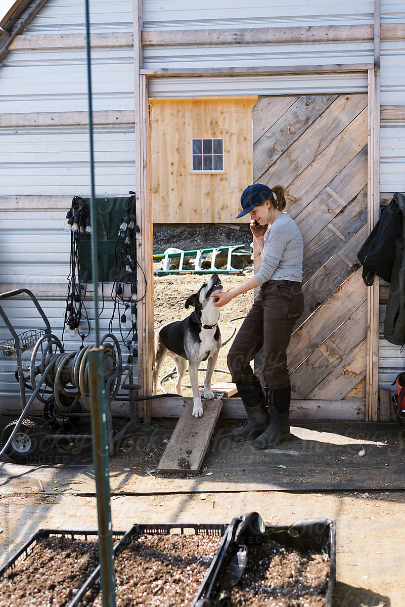 business owner standing with dog inside greenhouse having a phone call
