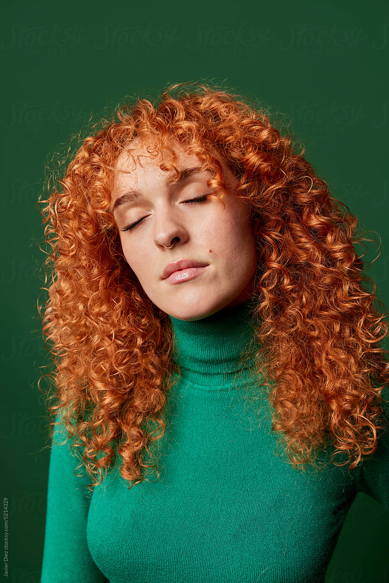 Tranquil young ginger woman on green background