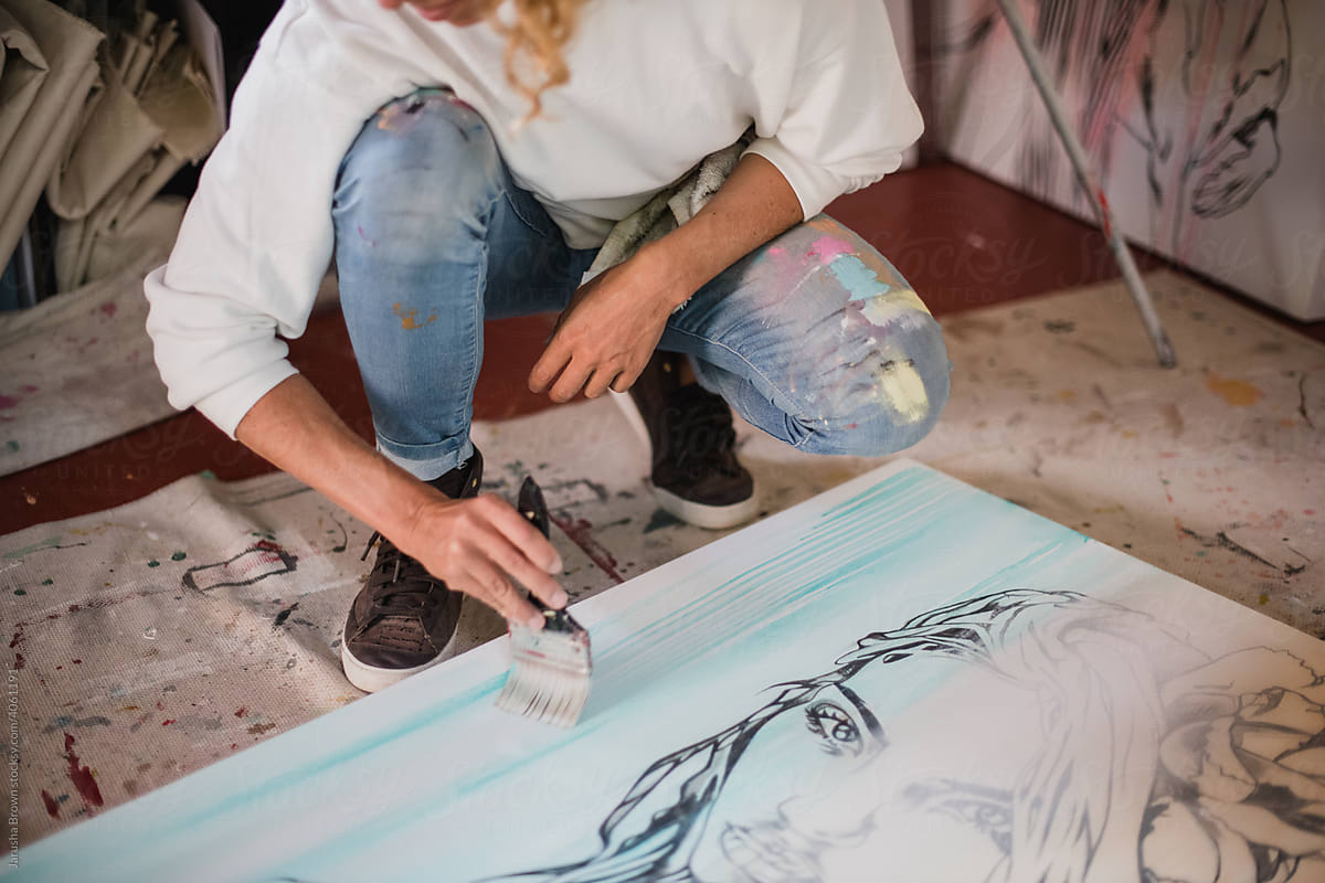 Woman squats down to paint a canvas.