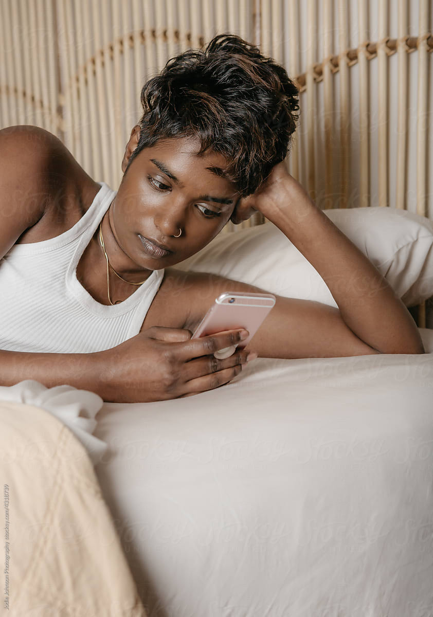 Multi racial young woman holding her cell phone in bed