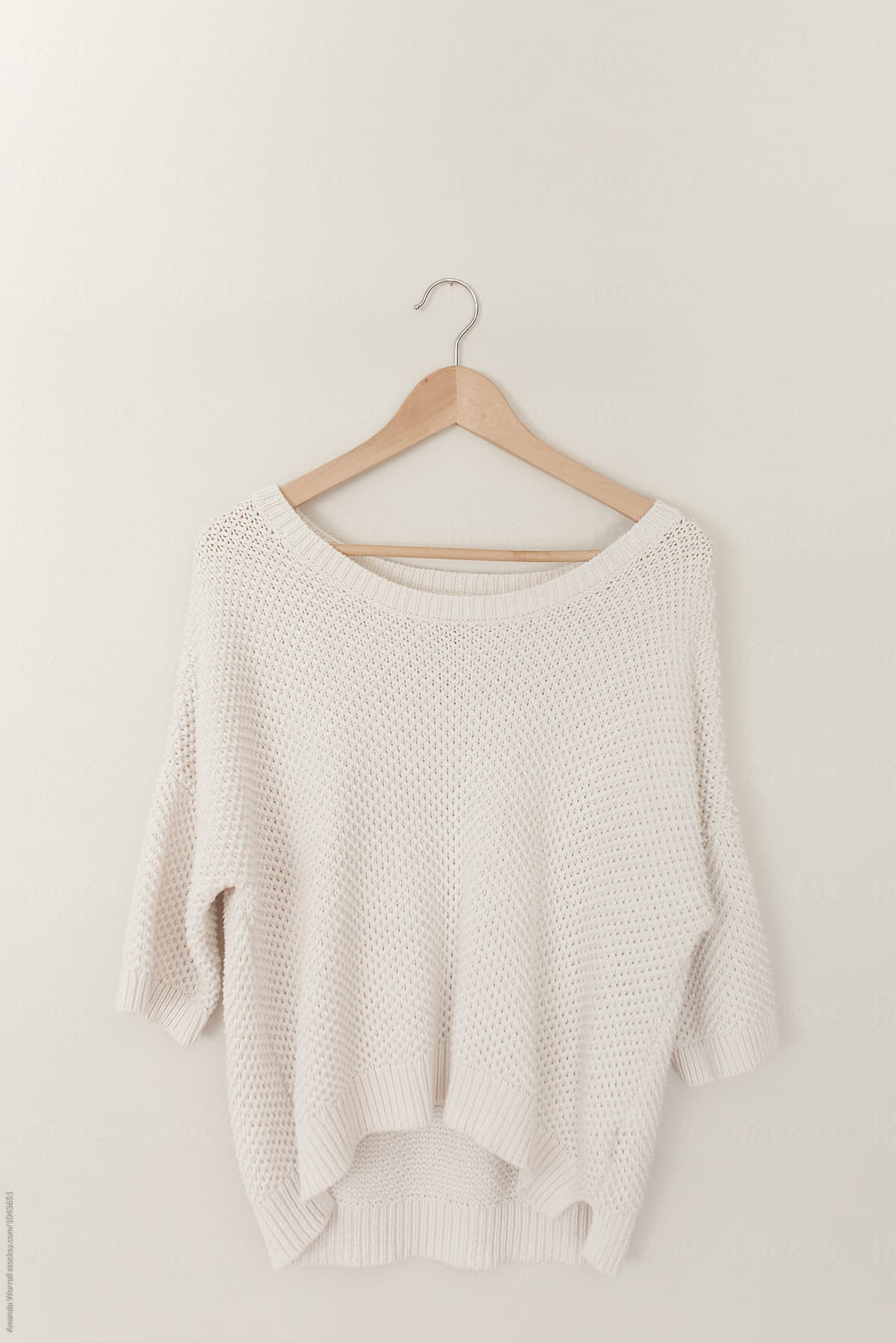A minimalist image of an off white sweater hanging on a wood hanger by ...