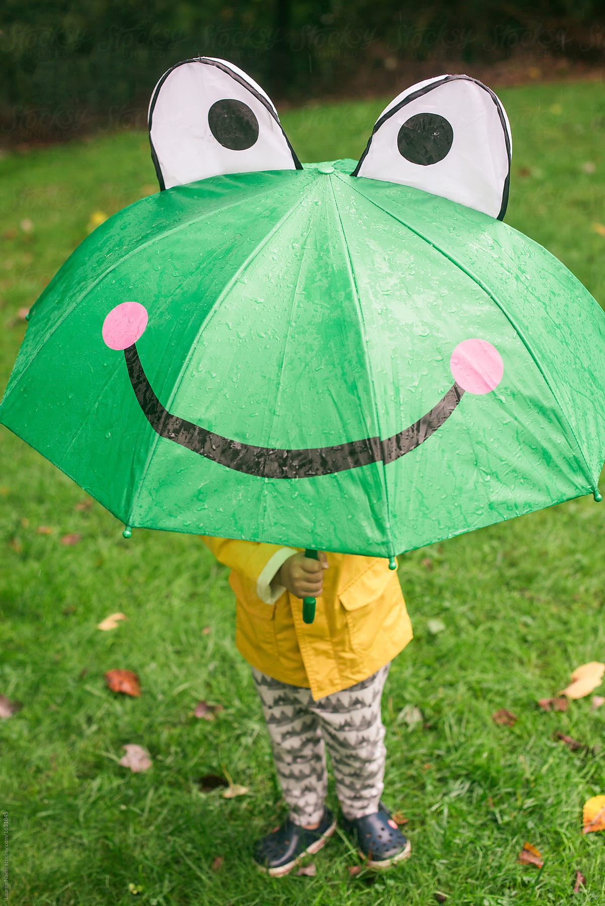 Little kid playing in the rain with umbrella