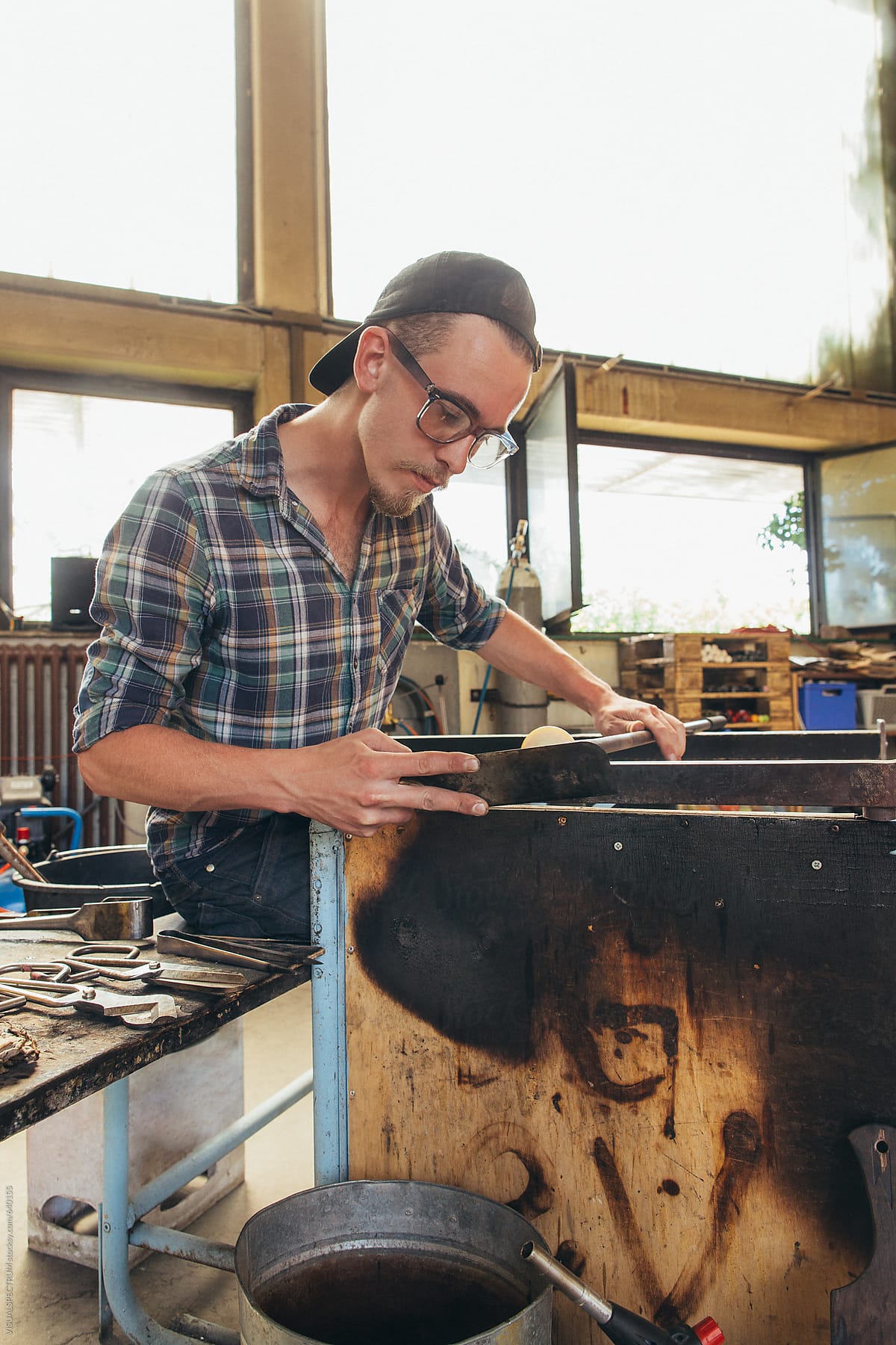 Artisan Glass Workshop - Portrait of Male Hipster Glass Artist Shaping Hot Glass With Metal Spatula