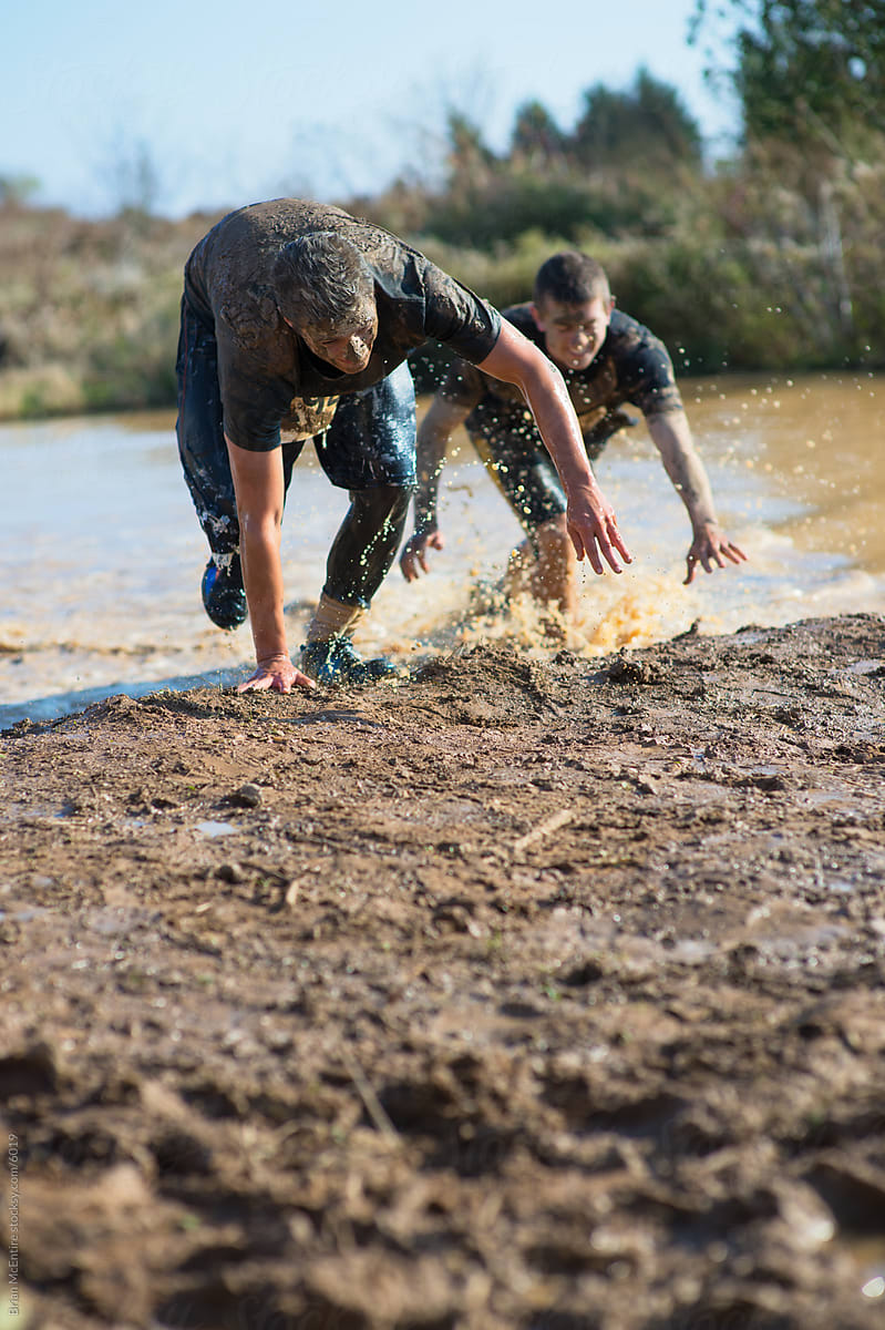 Two Men Run Through Water Obstacle on Mud Run Course