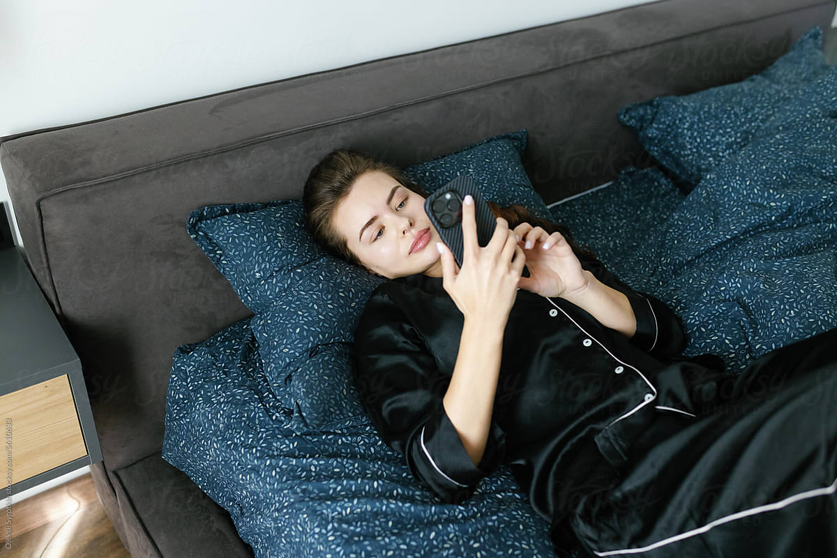 Young woman lying in bed using smartphone