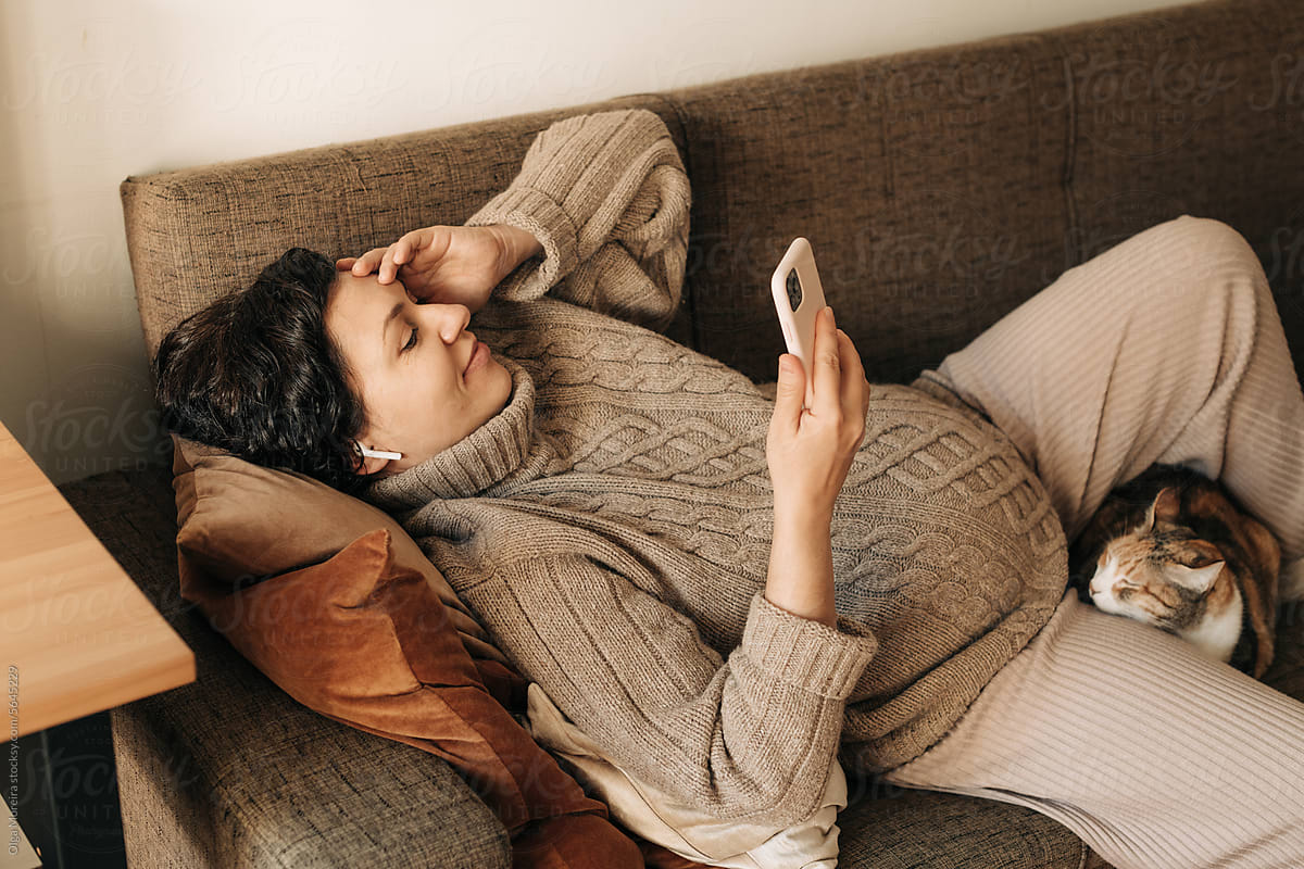Pregnant woman using phone resting on sofa at home