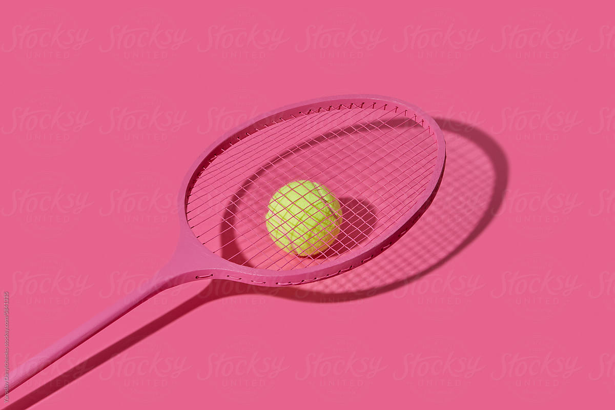 Tennis racket with yellow ball on pink studio background
