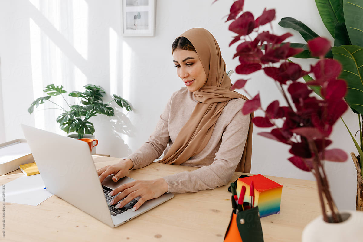 Content woman in hijab working with laptop in office
