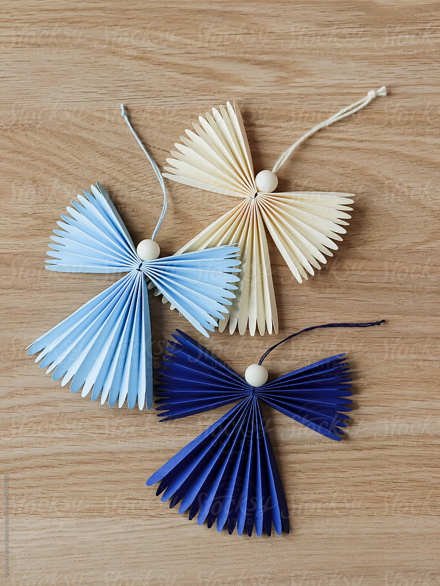 Three flying origami angels with cotton ropes on wooden background