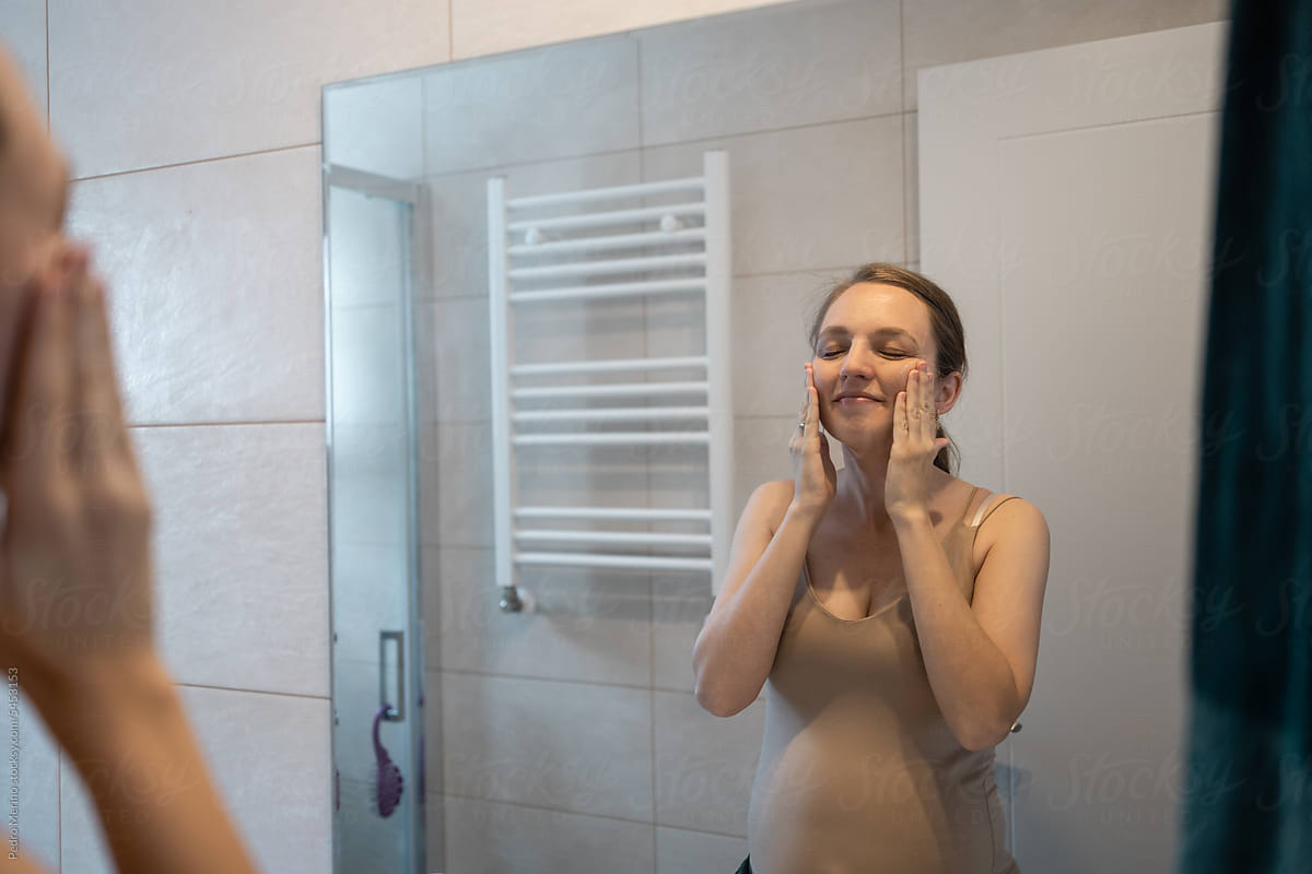 Pregnant woman doing skin care in bathroom at home