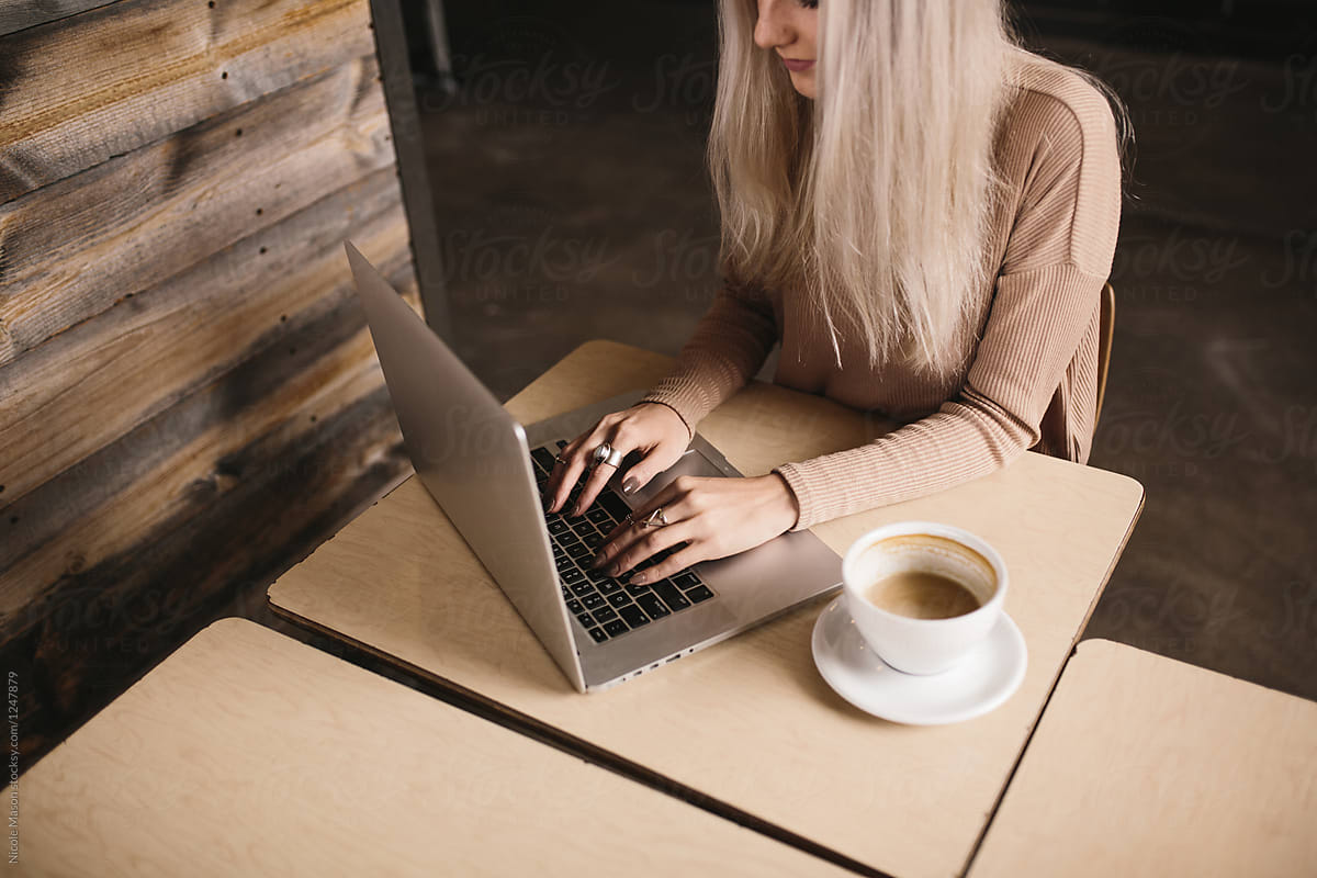 young woman typing at computer on desk in coffee shop