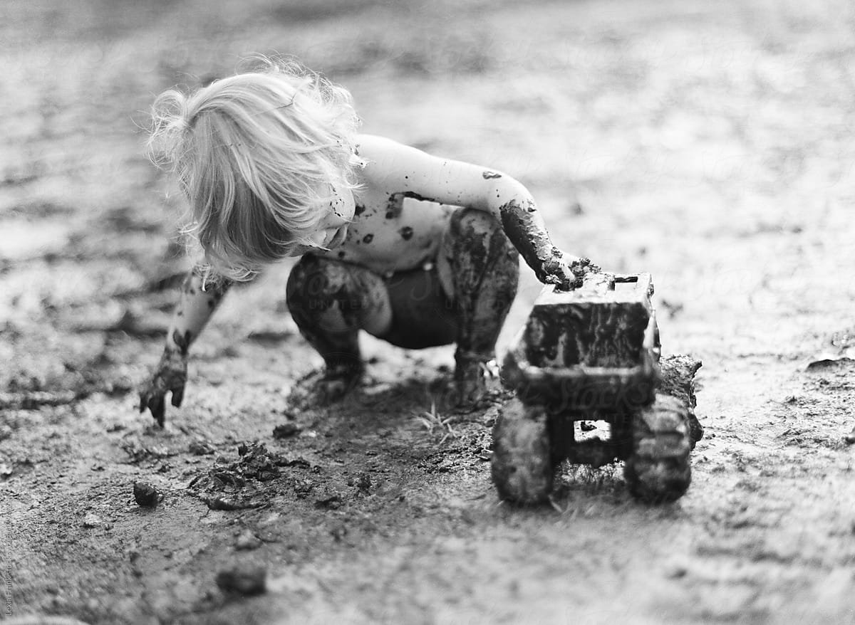 young child completely covered in mud playing with truck