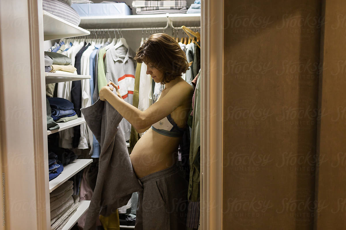 Pregnant woman putting on casual clothes at the wardrobe at home