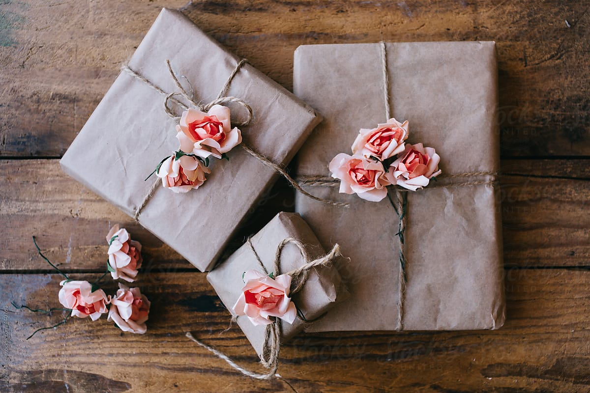 Three gifts wrapped in brown paper and decorated with pink flowers made from paper