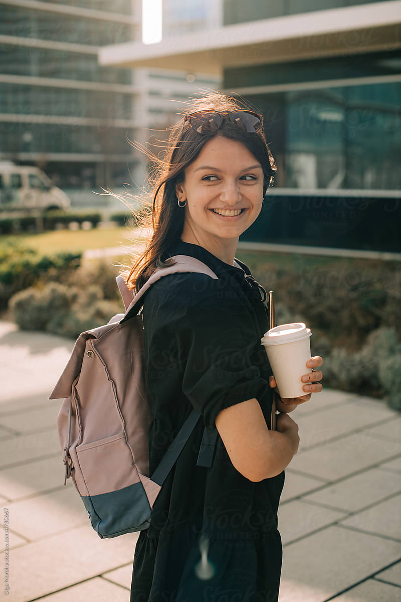 Smiling student with laptop and a cup of coffee to go