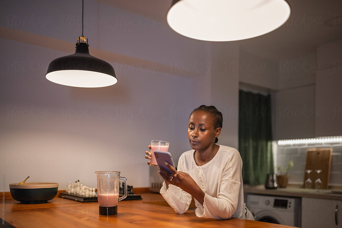 Black woman drinking smoothie and using smartphone