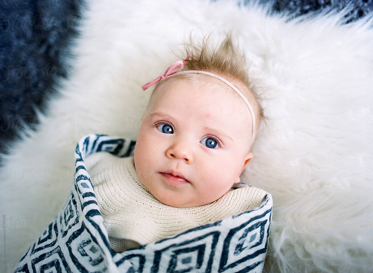 overhead view of blue eyed baby on white fur blanket