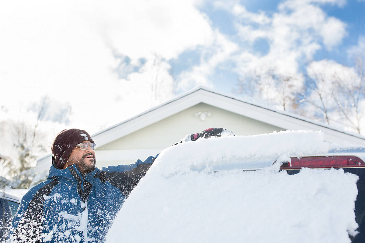 Black man sweeps snow off of vehicle