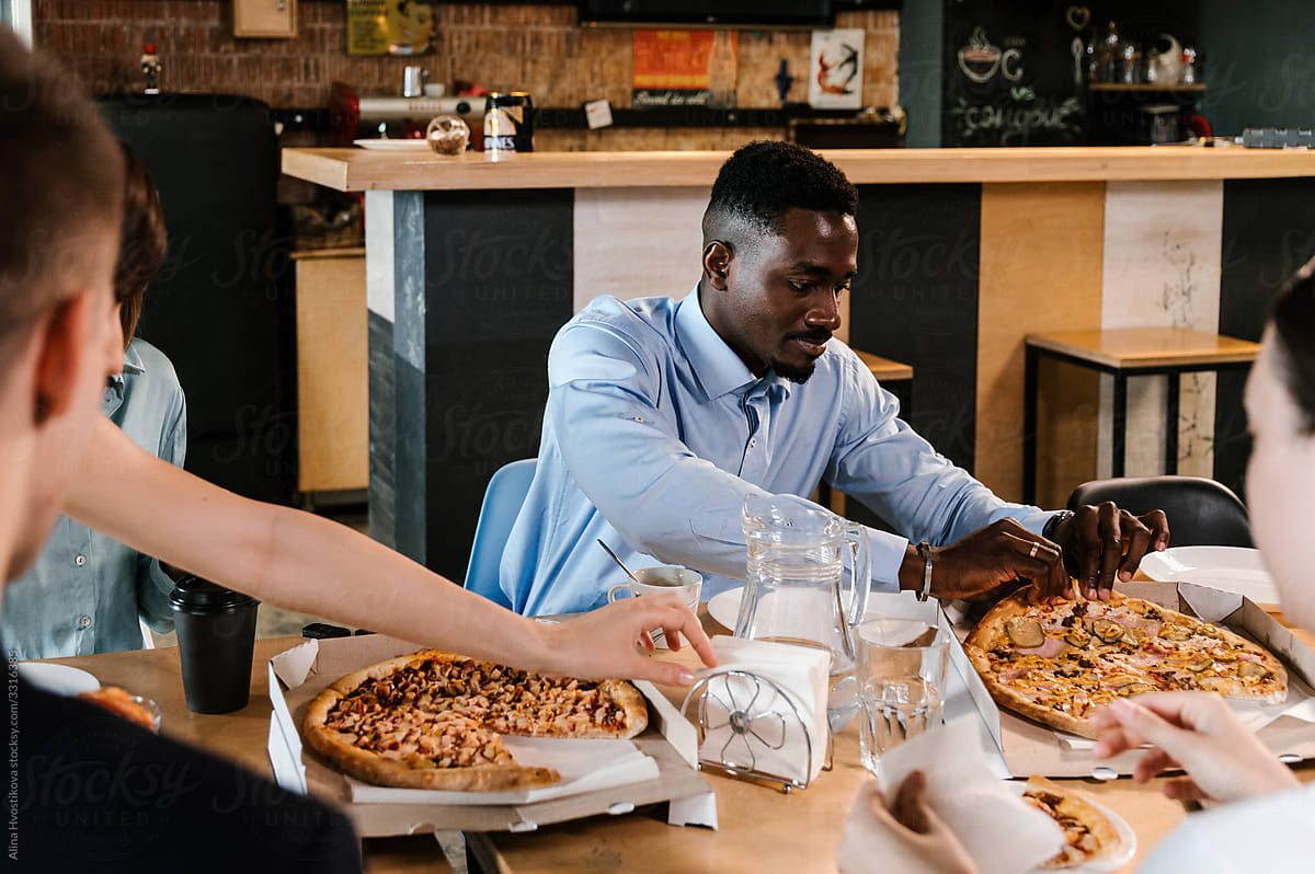Black man eating pizza with colleagues