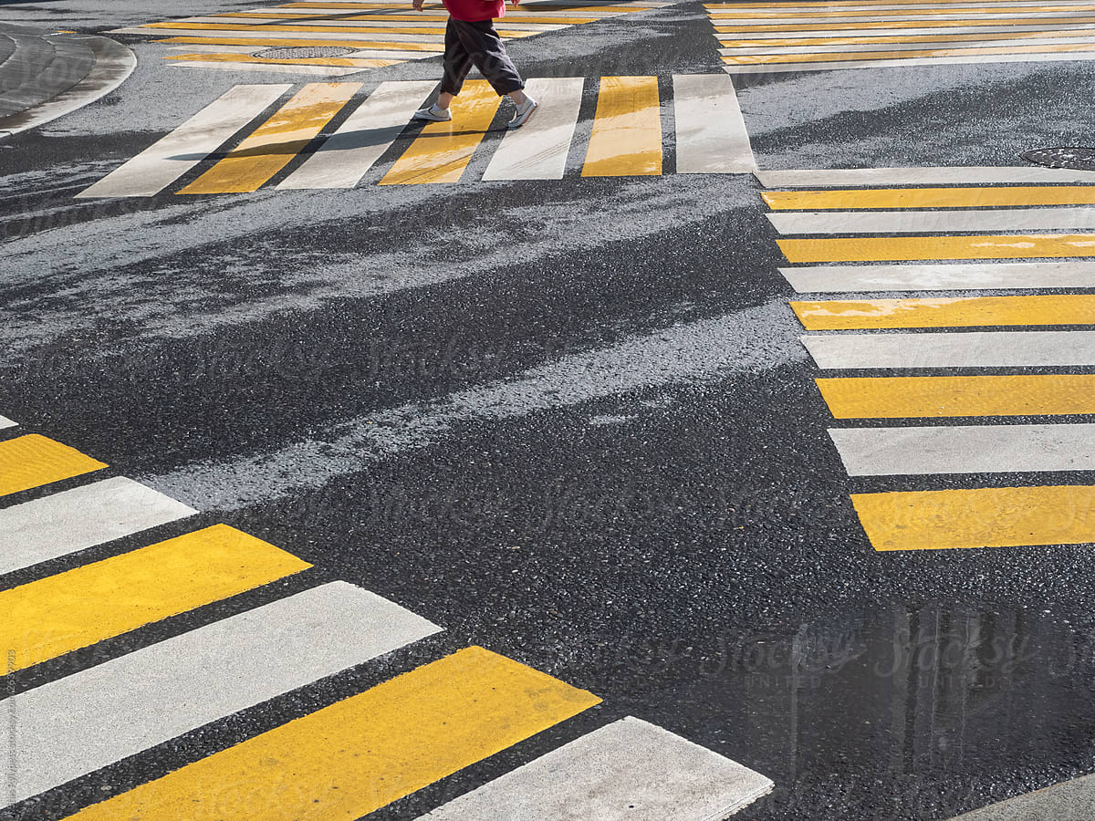 A pedestrian crosses the road on a yellow-white zebra crossing