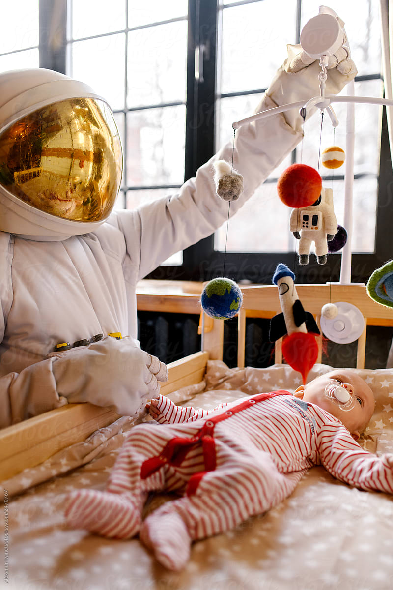 Person in spacesuit near baby in infant bed