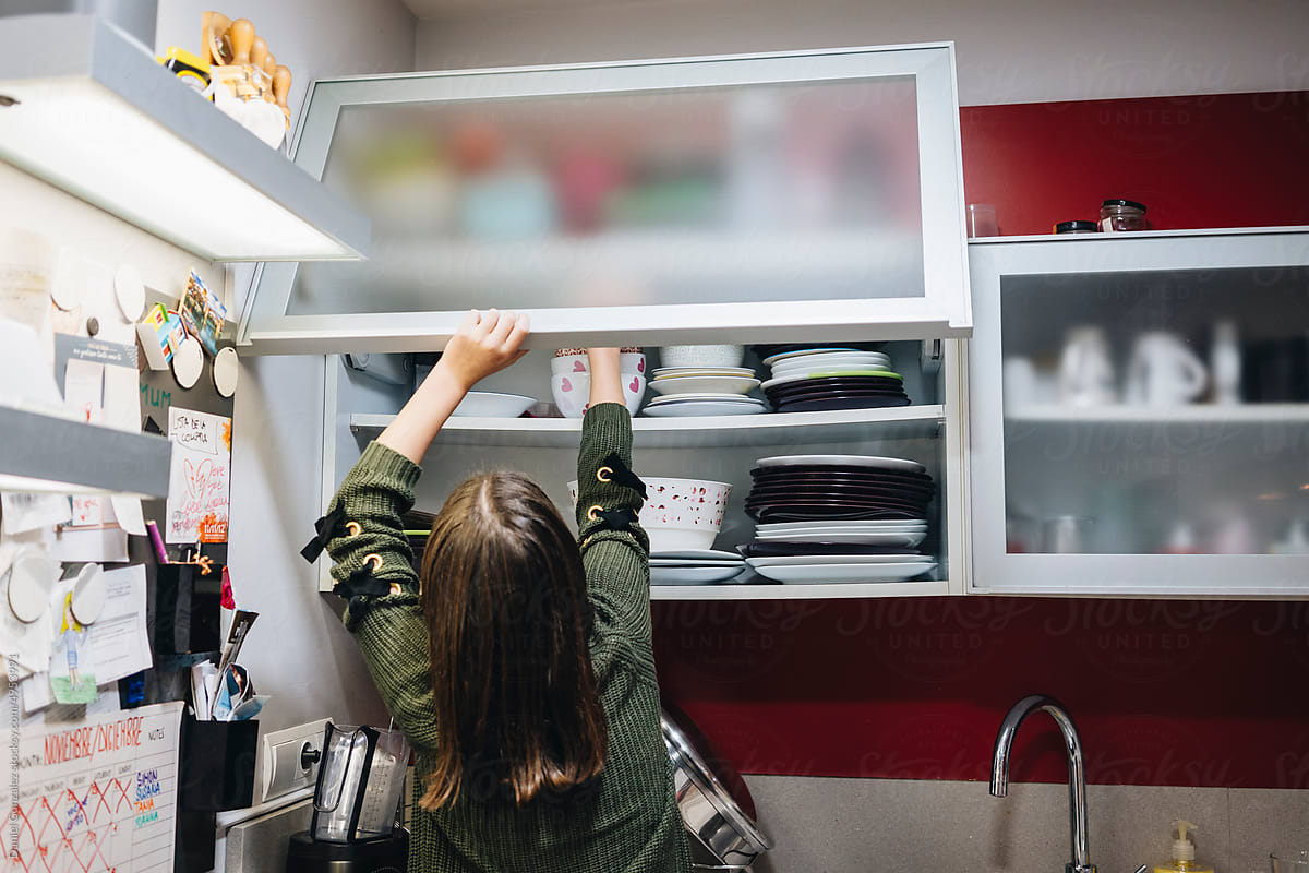 Girl taking dish from shelf in cupboard