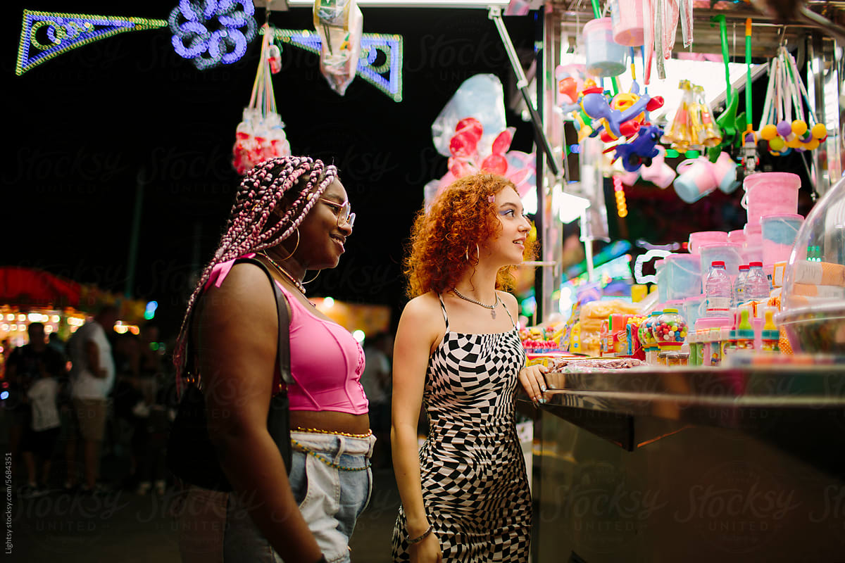 Young women buying cotton candy at a fair at night