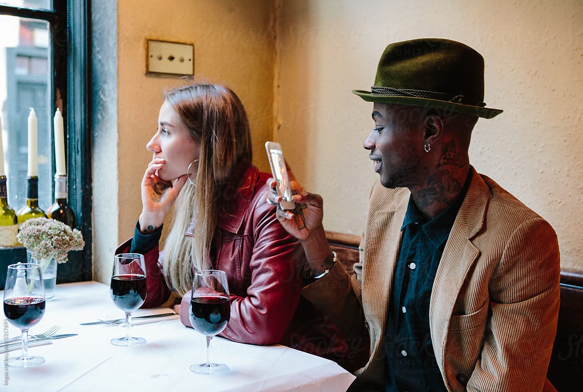 guy on a date staring at his phone, woman looks unhappy