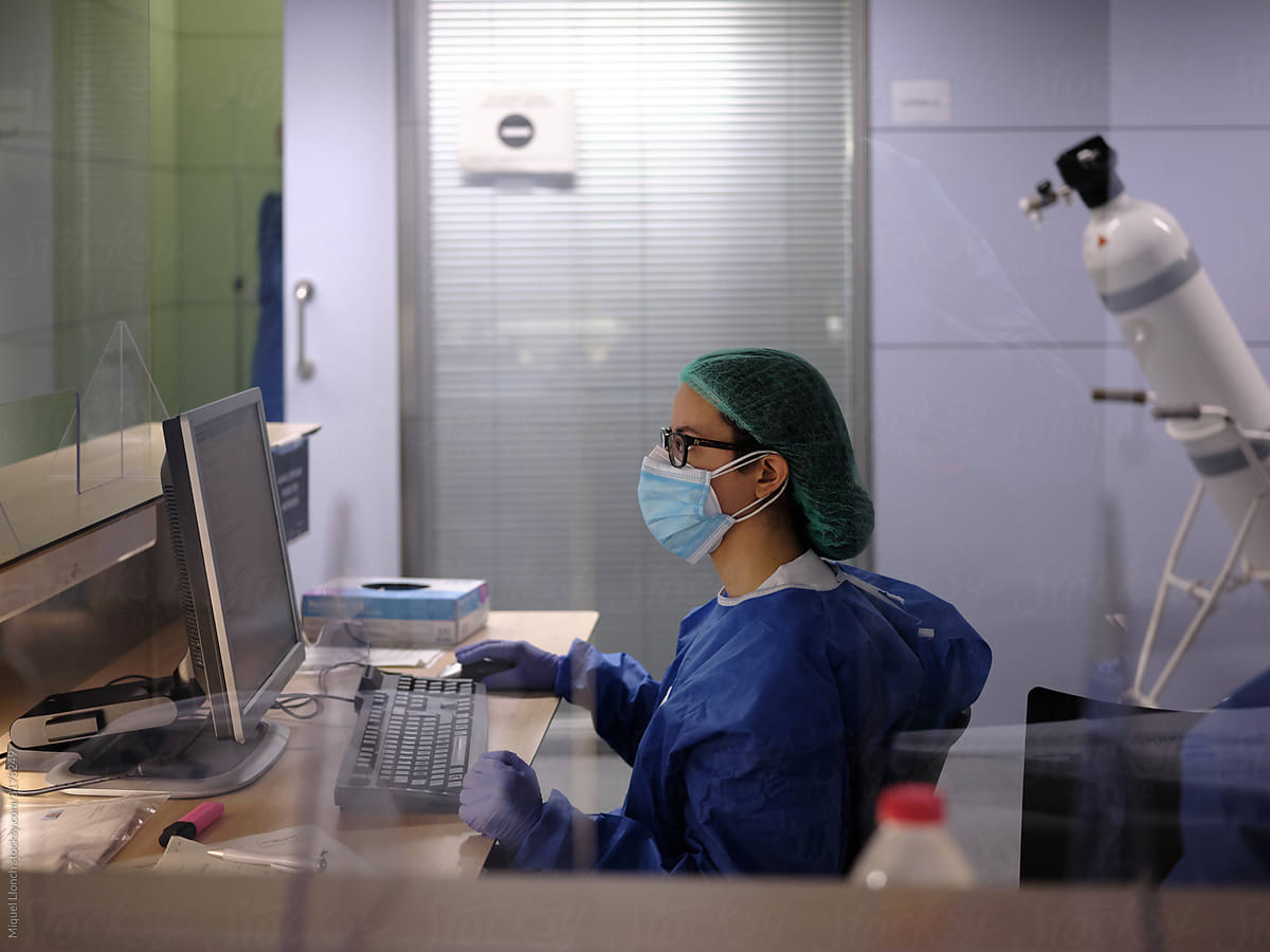 Female doctor dressed in scrubs and mask looking at computer monitor