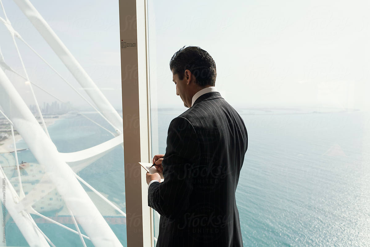 Businessman staring through window with skyscraper view, Dubai, United Arab Emirates