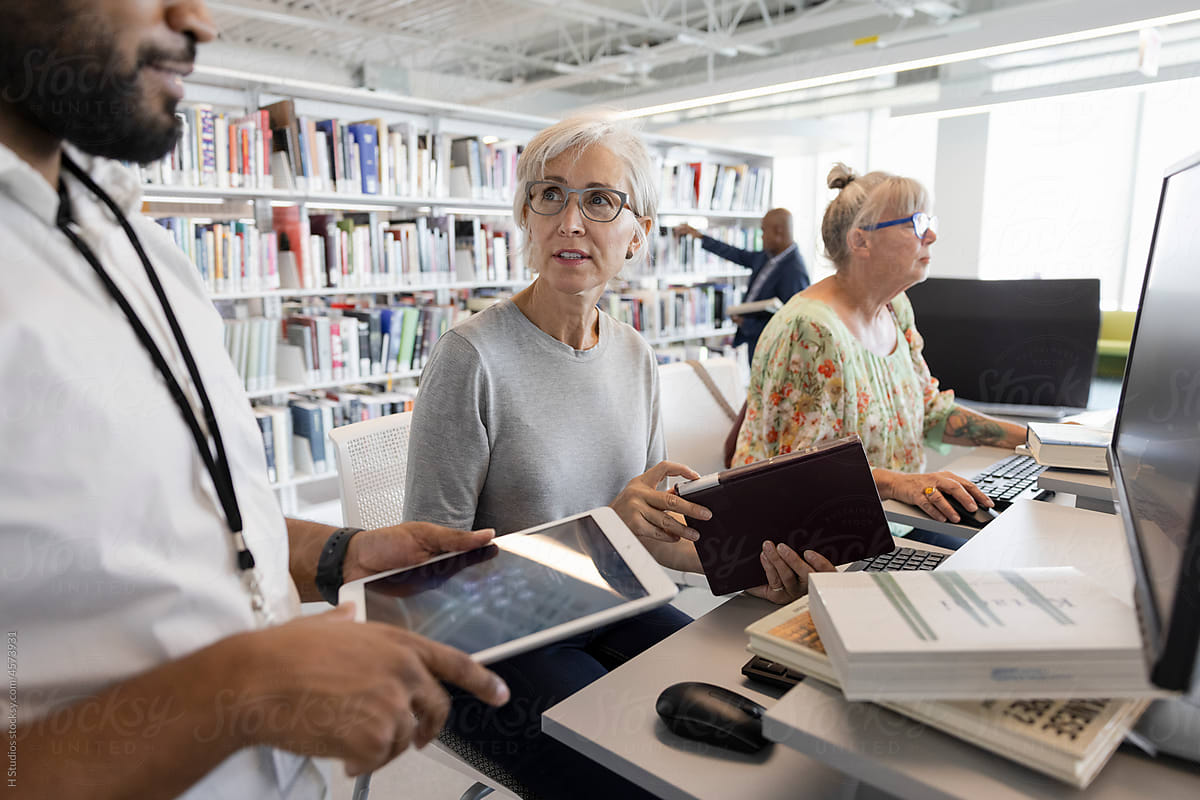 Librarian helping senior woman with books in library.