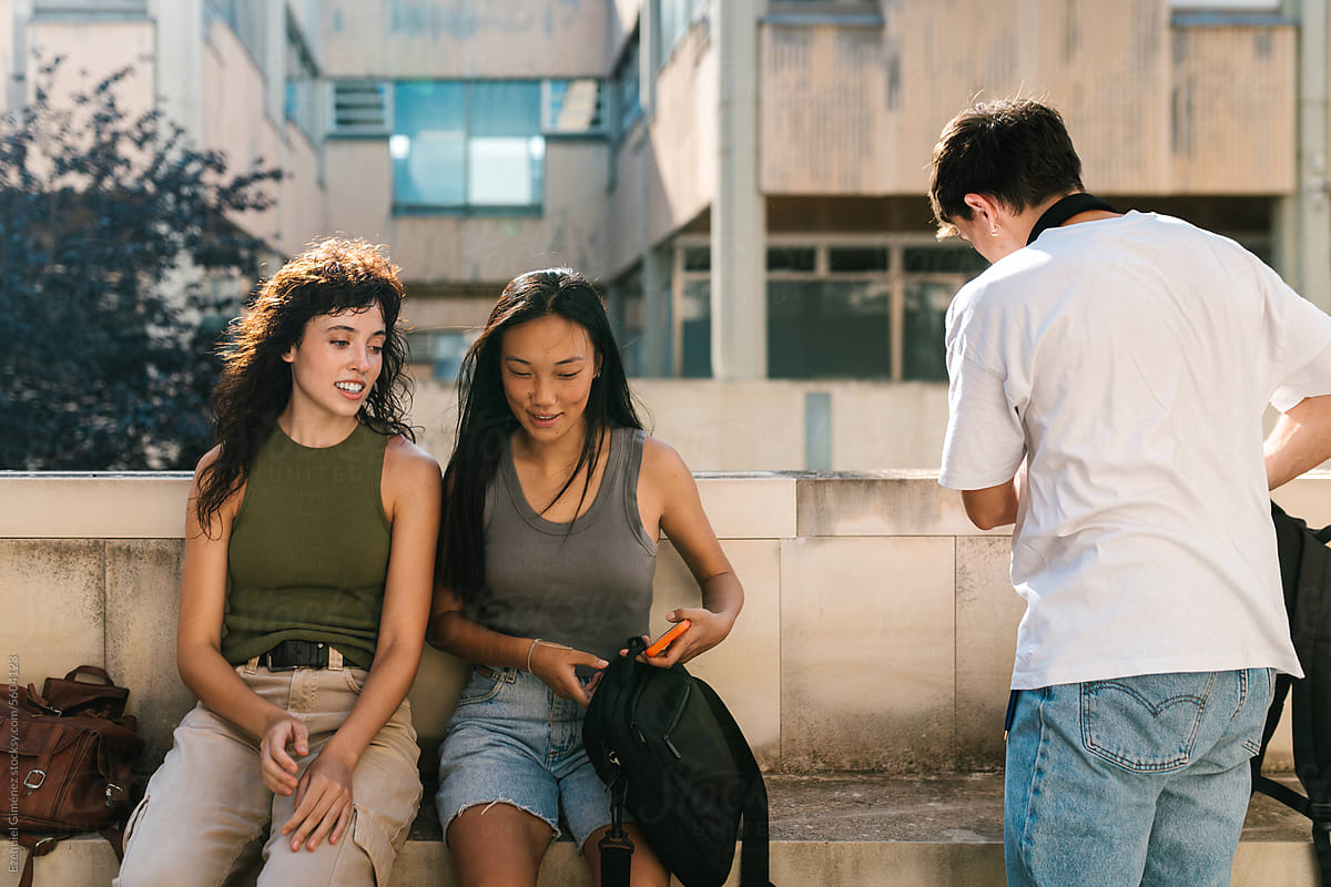 Cheerful multiethnic students sitting on street